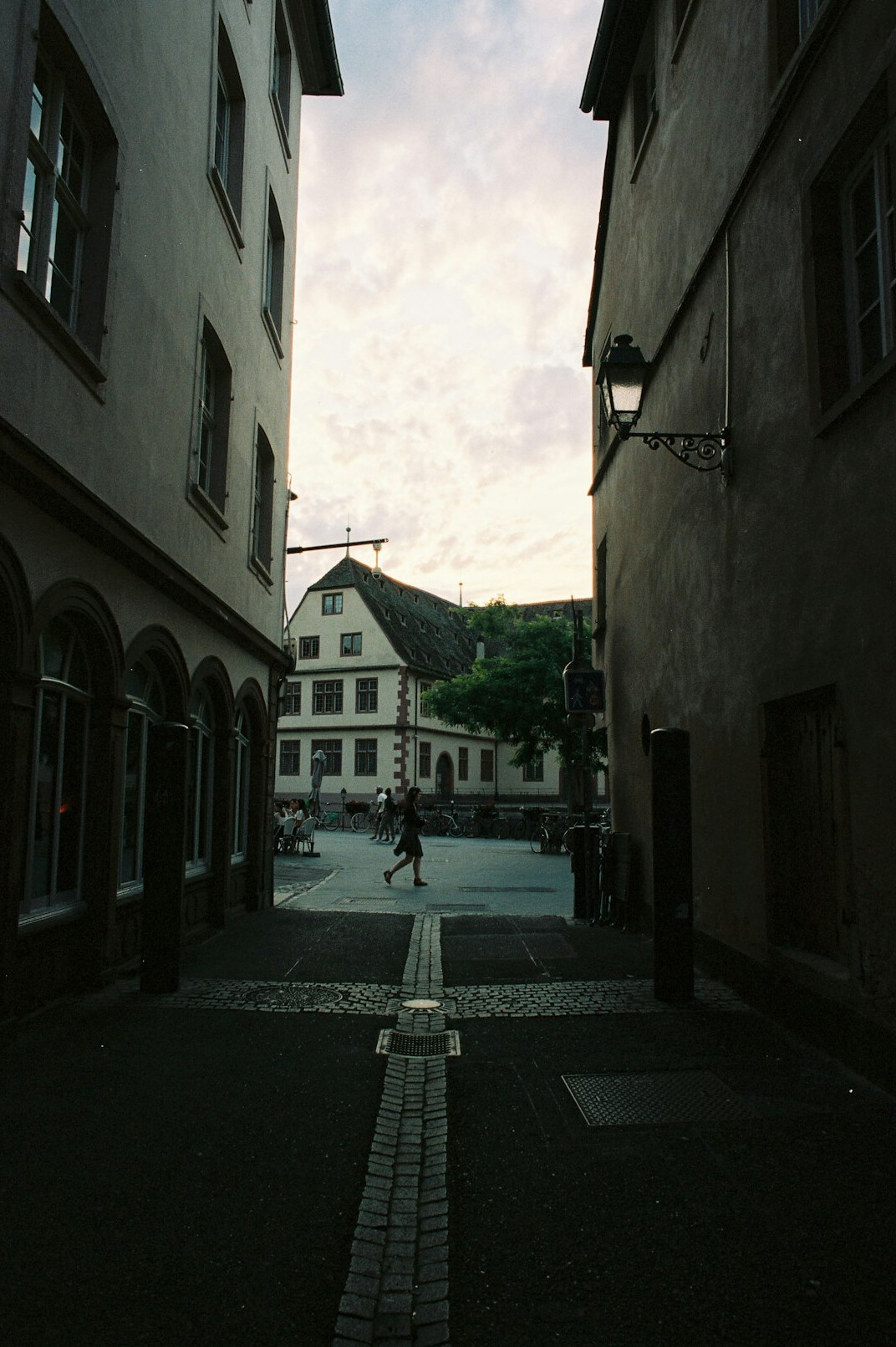 Quiet cobblestone European street at dawn with one distant figure walking away